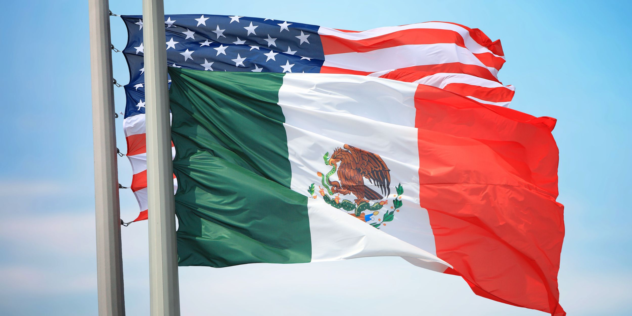 Flags of Mexico and USA against the background of a blue sky.